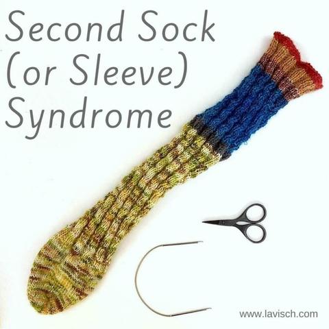 Flat lay view of a knit tube sock, together with a tiny circular needle and a small pair of scissors on a white background.