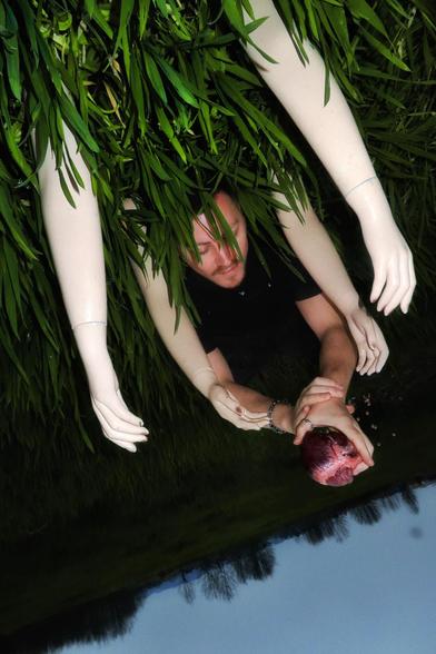 Nuño de la Serna lying on the ground holding a heart, reaching upwards with both hands, during a photoshoot in Sichuan, China