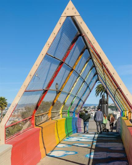 People walking through a triangular tunnel painted in rainbow colors