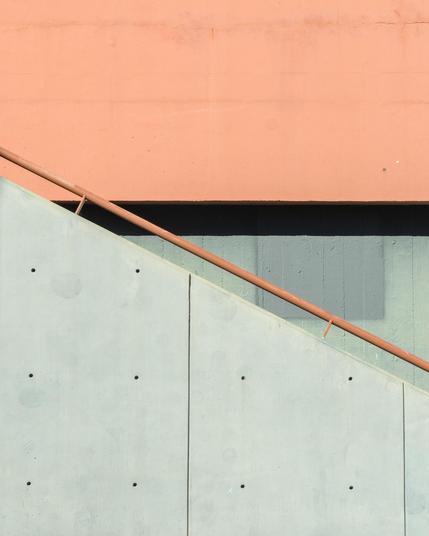 A minimalist shot of a concrete staircase, where the banisters make a triangle against the wall behind