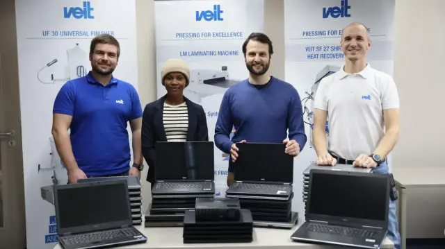 4 Personen, je 2 von der Fa. Veit und dem Hilfsverein für Tansania stehen vor Roll-Ups der Firma. Auf dem Tisch stehen mehrere Stapel an Laptops, teils aufgeklappt. Alle schauen in die Kamera. Namen und Details im verlinkten Artikel.