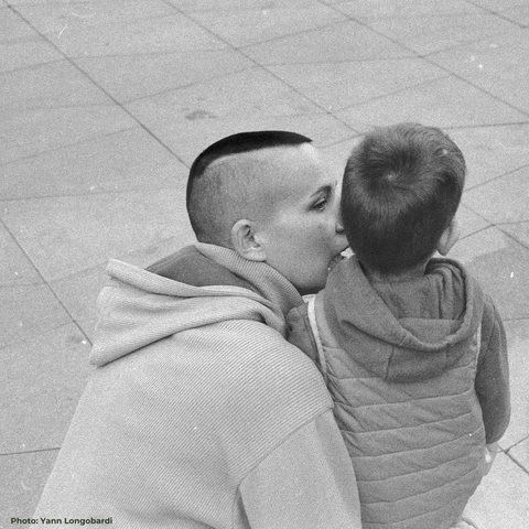Photo de Yann Longobardi, elle représente l'artiste et son enfant, la mère est accroupie à la hauteur de celui-ci,  et lui parle dans l'oreille,  l'enfant est de dos il regarde loin devant lui.