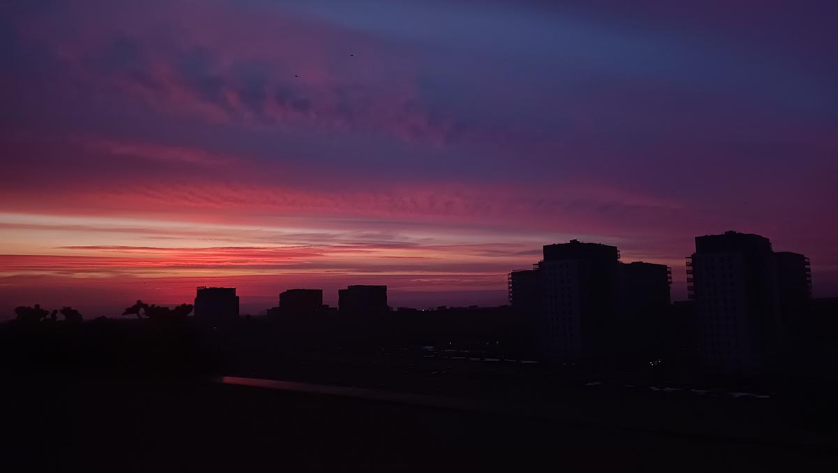 Widok na ciemną panoramę miasta tuż przed wschodem słońca. Na niebie jaśniejsze smugi chmur wybarwione odcieniami różu.