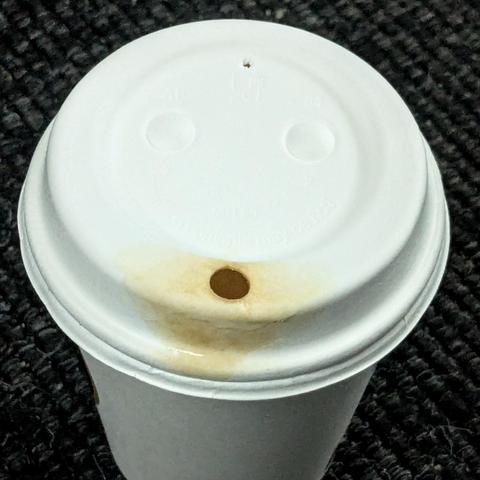 The lid on a coffee cup with two dimples and a drinking hole resembles a guilty face. The drinking hole is surrounded by a coffee stain, which could be likened to a chocolate stained mouth after gorging on chocolate cake.