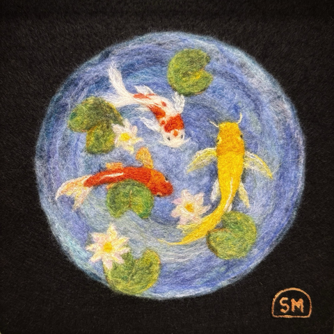 A circular needle felted koi pond on a black background. Three fish: one yellow, one orange and white, and one orange with white fins. Five lily pads and three lilies.