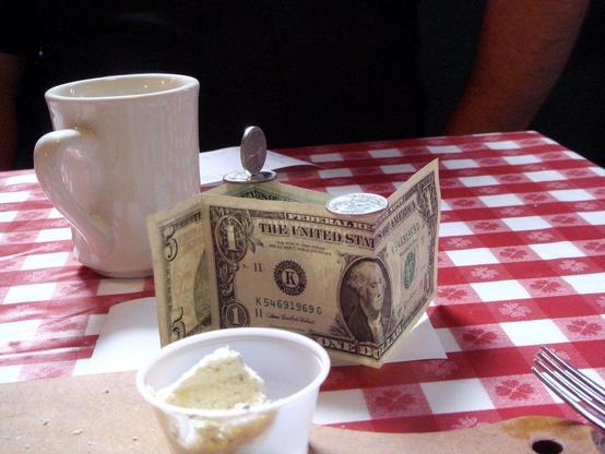 patron economy impact events: photograph of a cafe table with a red and white checked tablecloth, a coffee mug, fork, napkins, and a tip. Photo attribution: Flickr user cali2okie