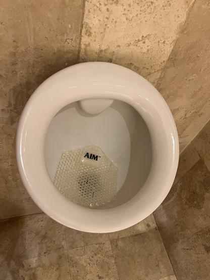 Small urinal with a plastic urinal screen/pad inside that has the word AIM printed on it