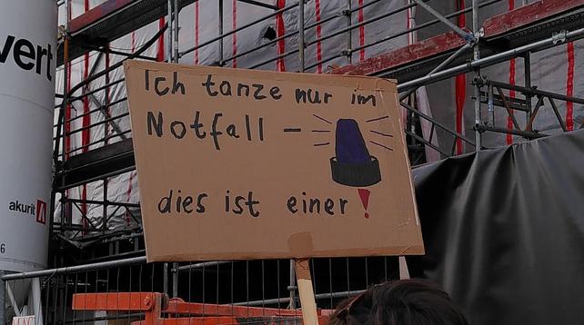 Demoschild mit der Aufschrift "Ich tanze nur im Notfall - dies ist einer!" Dazu ein handgemaltes Blaulicht. 