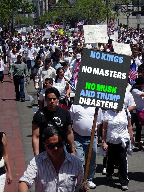 famous protestor Frank Chu leading a march and holding a sign saying NO KINGS / NO MASTERS / NO MUSK AND TRUMP DISASTERS