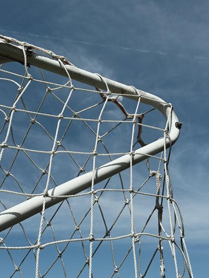 A close-up view of an outdoor soccer goal net set against a clear blue sky.
