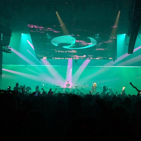 Area One, mit den Silhouetten feiernder Menschen im Vordergrund und Armin van Buuren am Mischpult im Zentrum des Scheinwerferlichts