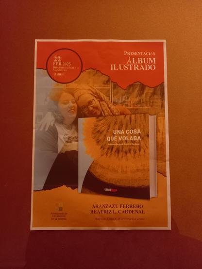 Foto al cartel que estaba en la biblioteca anunciando el evento de la presentación del álbum ilustrado “Una cosa que volaba” el 22 febrero a las 11 en la Biblioteca Pública Municipal Felipe Trigo de Villanueva de la Serena. Aparece una foto en la que salimos Aránzazu Ferrero y yo, y un mock up con el cuento. También aparece el logo del Ayuntamiento de Villanueva de la Serena.