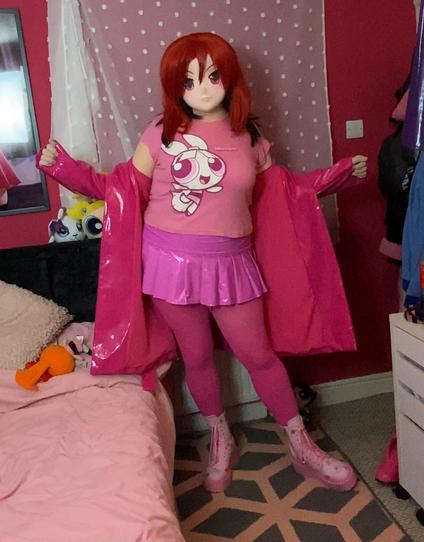 Kara Kig in a pink Powerpuff Tee that has Blossom on it. Kara is also wearing a pink PVC skirt and tights, with pink powerpuff boots and a Pink heavy PVC coat. All of the pinks don't match. 
