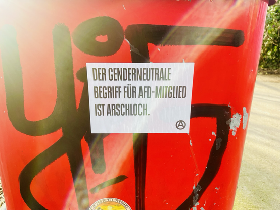Ein roter Mülleimer mit dem Aufkleber: der genderneutrale Begriff für Afd-Mitglied ist Arschloch