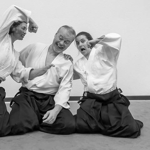 2 weibliche Aikidoka greifen einen männlichen Aikidoka in einem Scheingefecht an (kniend)