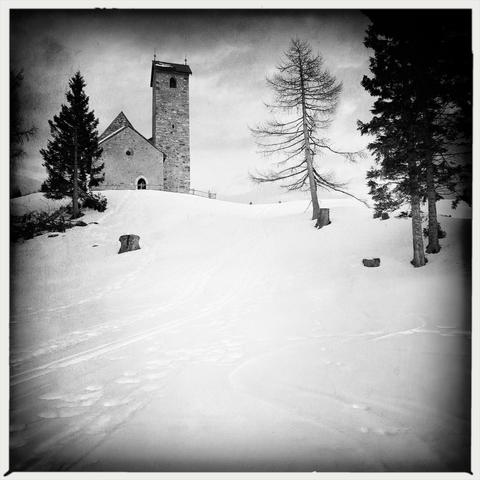 Una chiesetta su una collina innevata in montagna e alcuni alberi