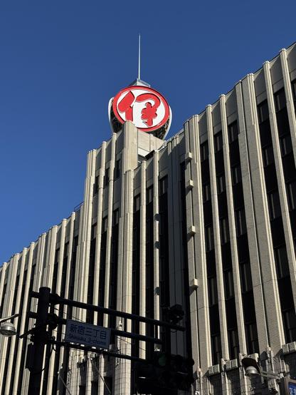 Bright blue skies perfectly framing the Isetan Department Store building in Shinjuku, Tokyo. The red company logo stands on top of the building, perfectly contrasting with the blue of the sky and the grey of the concrete below. 
