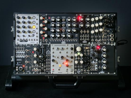 Two rows of Ukrainian modules in silver and black, inside a suitcase rig, featuring modules by Happy Nerding, Sitka, Crazy Chicken, Blukac, Dnipro, Endorphines and MachineRoom