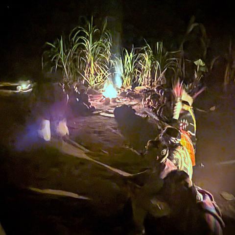 Huni Kuin people sitting near a fire outdoors, at night.