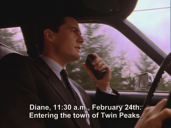 Agent Dale Cooper (Kyle MacLachlan) at the wheel of his car in the first episode of Twin Peaks. He speaks into his Dictaphone and says, "Diane, 11:30 am., February 24th. Entering the town of Twin Peaks".