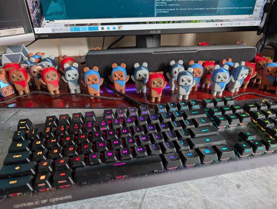 view of my keyboard in the bottom of my monitor on my desk showing a bunch like a bunch bunch of 3D printed ewoks. there's a variety of colors and styles but they are all standing there. aggressive looking with their claws up in the air demanding I accomplish something today.