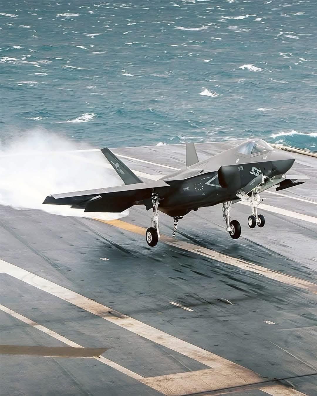 Un avion de chasse furtif F35 atterrit sur le pont d'un porte-avions, avec l'océan visible en arrière-plan. Un avion de chasse furtif F35 atterrit sur le pont d'un porte-avions, avec l'océan visible en arrière-plan.