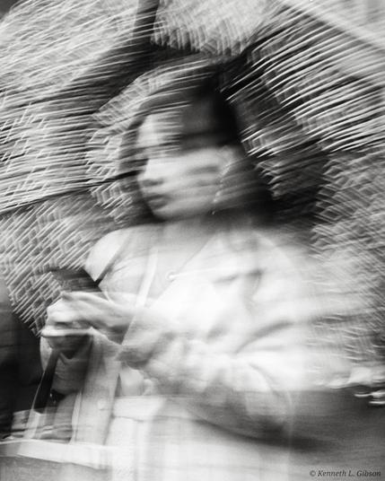 Monochrome intentional camera movement image of a woman with an umbrella and holding a phone.