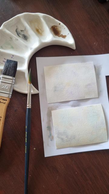 English 2 small rectangles of paper are laid out on a table and have light colors applied in watercolor (brown, beige, green, purple). There's a brush on the side and a ceramic palette in the shape of a crescent moon with the colors used.
•
Français 2 petits rectangles de papier sont posés sur une table et ont des couleurs légères appliquées à l'aquarelle (marron, beige, vert, violet). Il y a un pinceau sur le côté et une palette en céramique en forme de croissant de lune avec les couleurs utilisées.