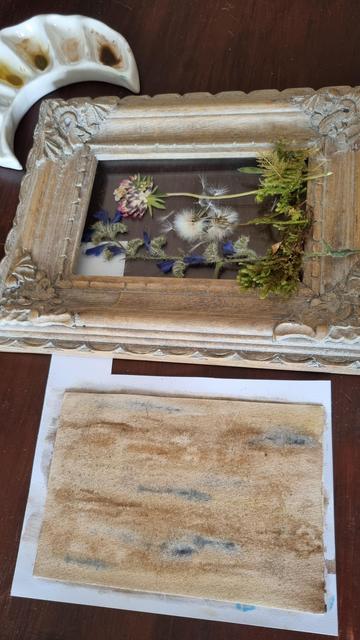 English We find the crescent-shaped palette at the top, then another larger gray-beige frame, with more flowers and mosses on top. A rectangle of paper at the bottom of the picture is painted in colors reminiscent of light wood.
•
Français On retrouve la palette en forme de croissant de lune en haut, puis un autre cadre, plus grand, couleur gris-beige, avec d'autres fleurs et mousses posées dessus. Un rectangle de papier en bas de l'image est peint de couleurs faisant penser à du bois clair.