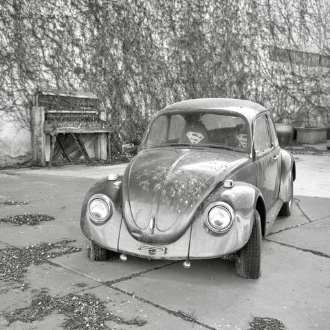 A black and white film photo. An old Volkswagen bug and weathered piano sit quietly outside in Lubbock, Texas. Sunday, February 16, 2025.