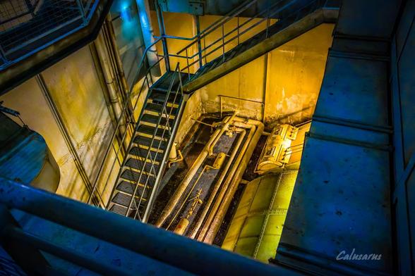 Une photo industrielle : des escaliers qui descendent au fond d'une fosse carrée. 