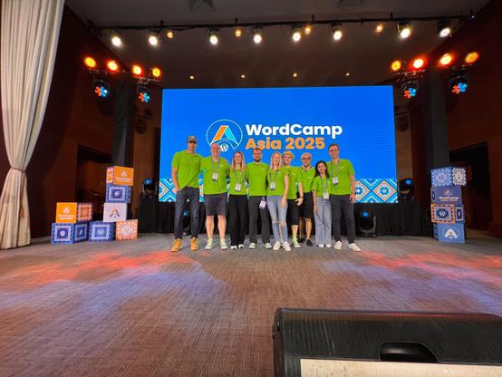The Syde team in matching green shirts stands on stage at WordCamp Asia 2025 in front of a large screen displaying the event logo. The team is smiling and posing for a group photo.