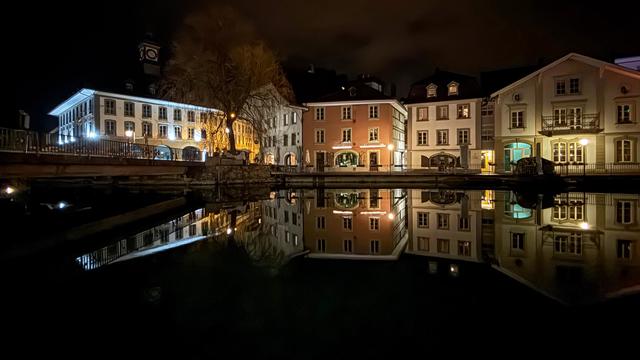 Nachtaufnahme einer Häuserfront, die sich im Wasser spiegelt. 