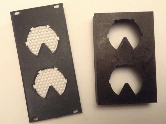 Photo of two 3D printed enclosures reproducing the shapes of the Krell displays in the 1950s Sci-Fi film Forbidden Planet.  On the right is my previous attempt, now with the actual display panels removed.  On the left is a 12HP EuroRack format panel with two Krell displays, one above the other, each of which is a circular shape with one sixth removed at the bottom in a "pacman-but-facing-down" type effect.  The frame and panel are black, the two displays themselves are white.
