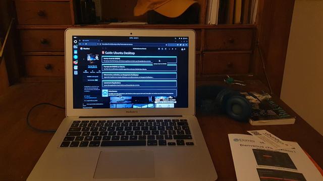 un ordinateur ultra portable, de la marque à la pomme croquée, avec le logiciel d'exploitation Ubuntu, un casque audio, un livre de poésie, une brochure de démarrage rapide 