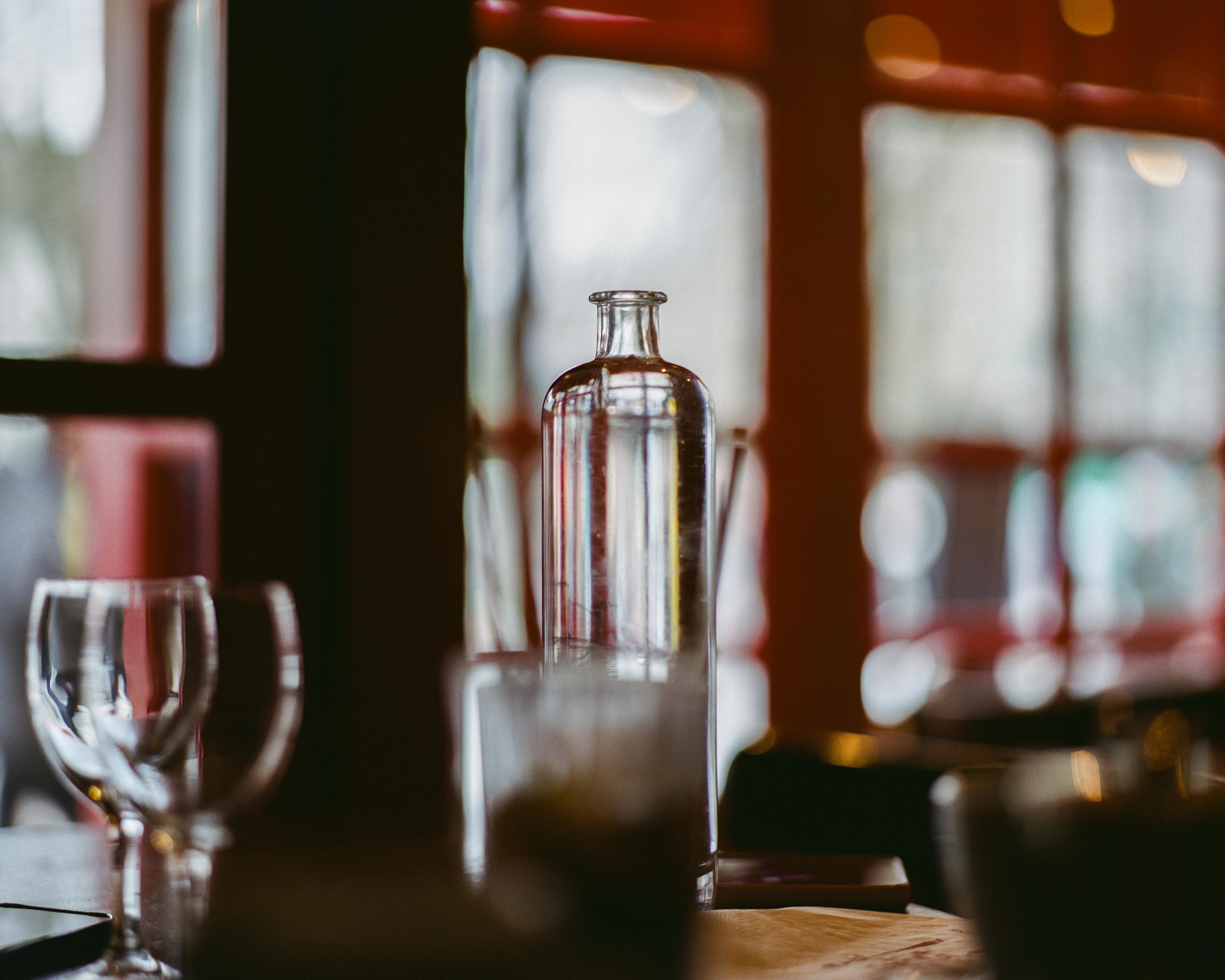 A perfectly straight glass bottle filled with water, refracting the paned windows behind it.