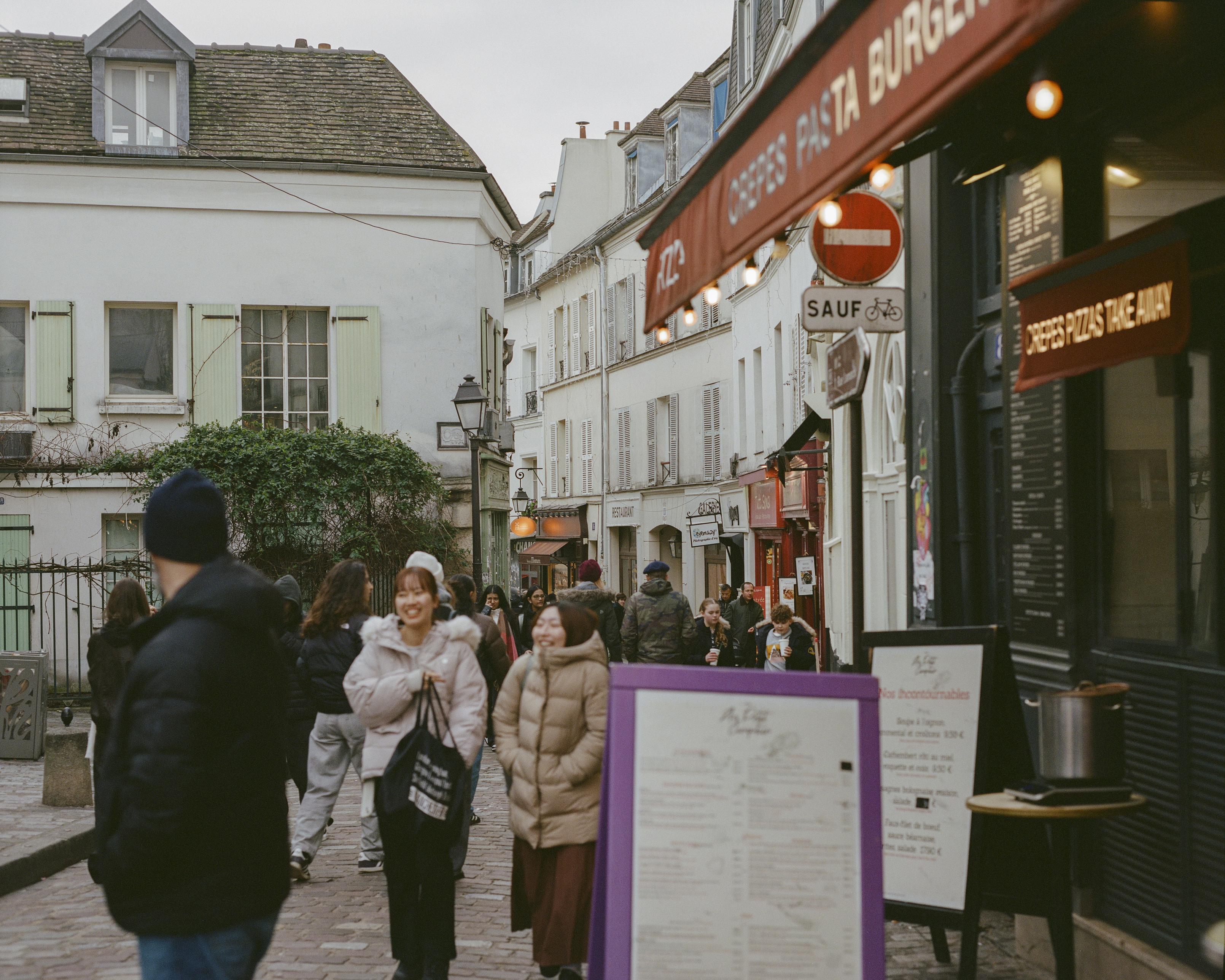 A Parisian street with cafés and boutique shops on an overcast day, people walking down the middle.