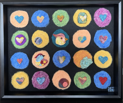 20 felted circles mounted on black felt in a black frame in a 4 down and 5 across grid: peach, blue, green, yellow, teal, and orange. Each circle holds another colourful felted shape or shapes: hearts, birds, flowers, circles.