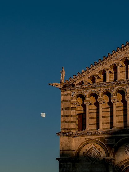 Una statua del duomo di Pisa è affiancata dalla luna durante il tramonto.