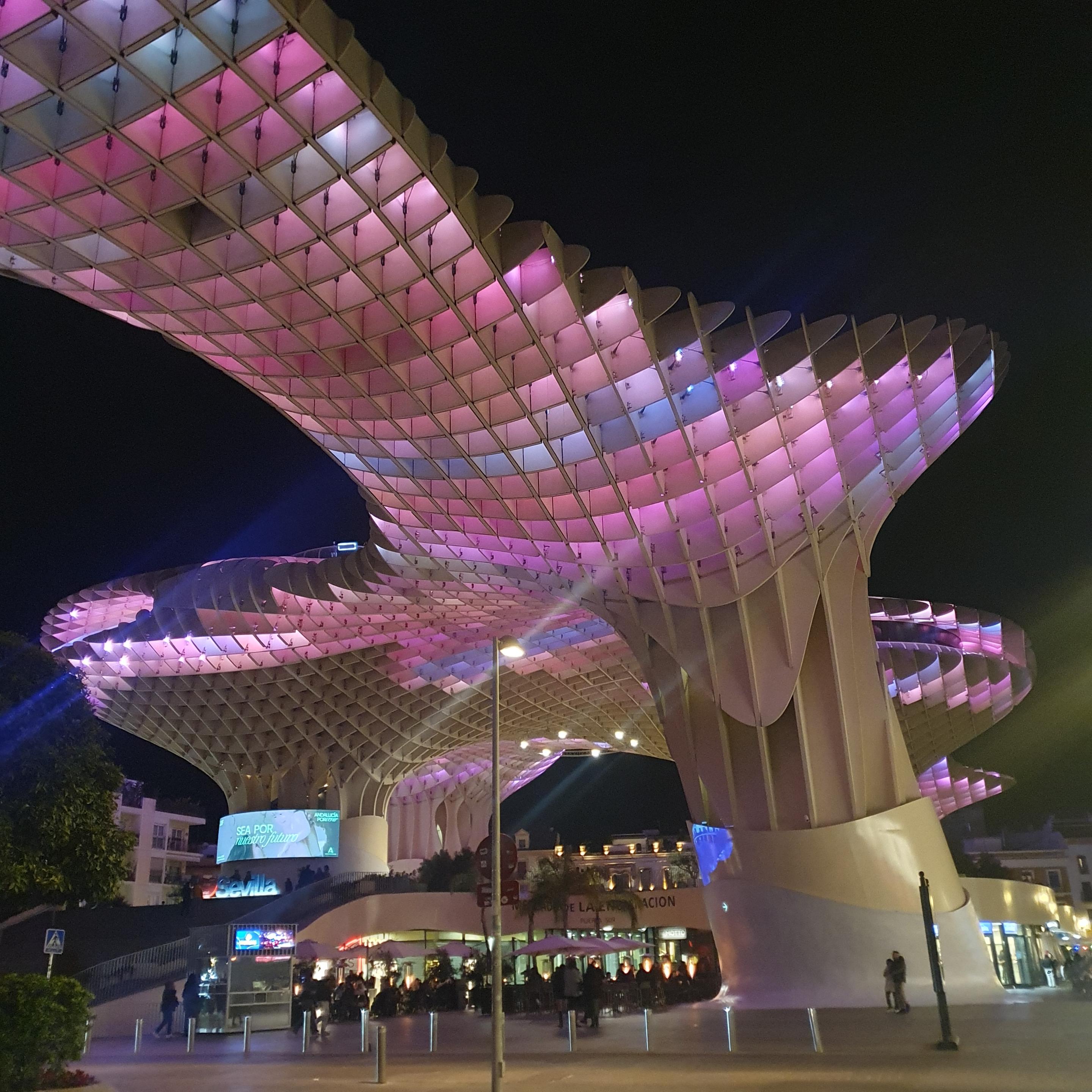 A giant wooden structure above a plaze, bathed in pink and purple lights. The whole thing looks very surreal. . 