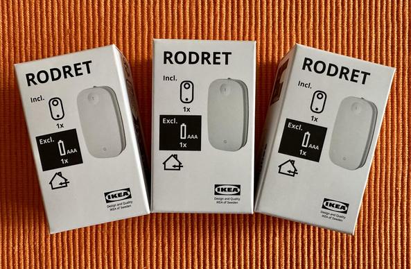 Three boxes of IKEA's RODRET product, labeled with contents information and battery requirements, placed on an orange textured surface.