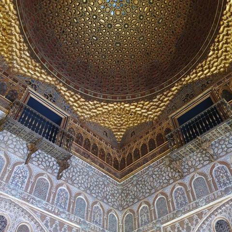 Looking up towards a beautiful cupola ceiling in a palace with walls full of elaborate decorations in blue and gold. It looks Islamic but also but clearly is now as some humans are shown. 