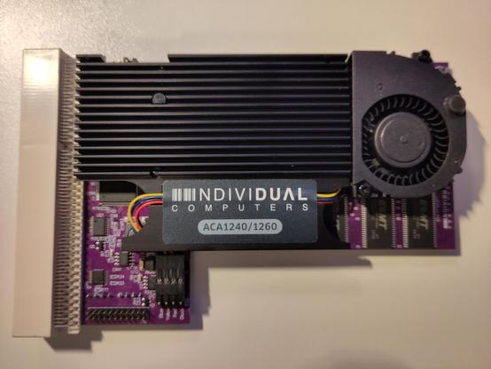 ACA1260 bottom side, purple PCB, white Amiga 1200 edge connector,  with big black heatsink on the '060 and a radial fan to blow air on it from the side. There's an Individual Computers ACA1240/1260 sticker on the heatsink, holding some cable in place.
