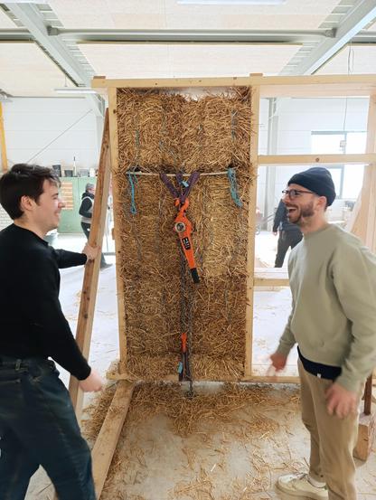 2 carpenters having fun learning straw building. Straw vale timber module with chain hoists  to add pressure in the background.