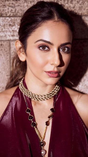 In her latest appearance, Rakul Preet Singh stunned in a burgundy floor-length gown that exuded luxury and elegance. The metallic draped dress featured a sophisticated halter neck with a plunging neckline and a sensual thigh-high slit, perfectly accentuating her figure. Paired with bold gold accessories and styled by Anshika Verma, Rakul's ensemble has become the talk of the fashion world.