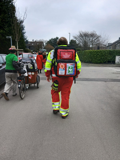 Ein Demosanitäter am Ende der Demo mit einem Rettungsrucksack läuft dem Karnevalszug hinterher, noch ist nicht viel los, hier im Bild ist die aufstellphase zu sehen, die Menschen stehen weiter vorne.
