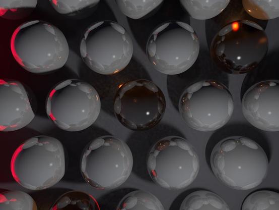A 3D rendering made with raytracing, utilising radiosity and photons, of a series of reflective grey spheres and mirrored orange glass spheres, arranged in an offset grid pattern.  A bright red accent reflects on some of them on the left side.