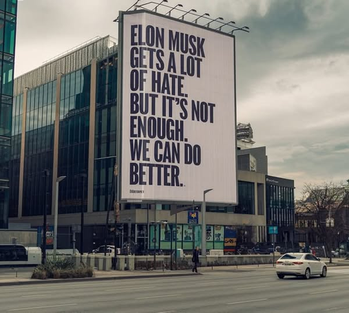 Pic of a billboard on the side of a building:
ELON MUSK
GETS A LOT OF HATE 
BUT IT'S NOT
ENOUGH. WE CAN DO
BETTER.