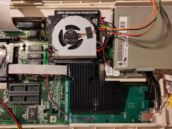 Upper view of an opened Amiga 1200 with a Warp1260 accelerator installed. The radial fan cooling solution is next to the floppy drive, near the wide part of the trapdoor slot, towards the back of the machine. It blows air onto a black wedge-shaped large heatsink mounted on the '060.