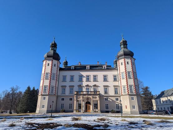 Château de Vrchlabí de style baroque, bien entretenu. Un peu de neige fond doucement au soleil sur l'enceinte du château. Grand ciel bleu.
